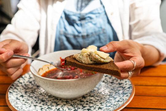 Cropped view of a person holding dark rye bread with lard spread and garlic while eating borscht