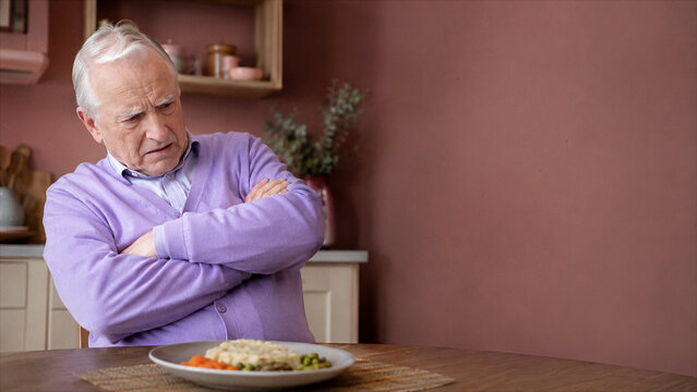Depressed elderly man refusing food at dining table, isolation and mental health