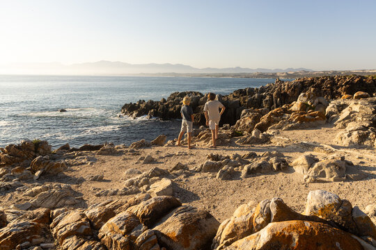 barefoot pre teen boys climbing and exploring the rocky coastline of DeKelders, South Africa