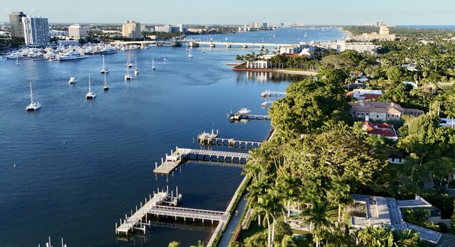 Aerial view of the Intracoastal Waterway with luxury yachts, private docks, and lush waterfront estates under a clear blue sky in Palm Beach, Florida, United States.