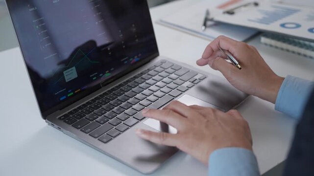 Professional financial analyst typing on a laptop and using the trackpad to review business performance data, charts, and graphs