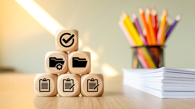 A close-up photograph of wooden blocks with business icons on a desk with office supplies.