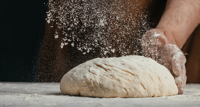 Baker dusting bread dough with flour during shaping process