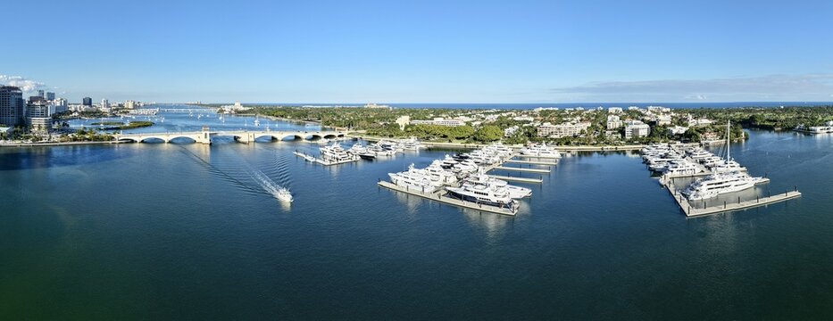 Aerial view of luxury yachts at a marina along the Intracoastal Waterway with the Flagler Memorial Bridge and lush coastal landscape in Palm Beach, Florida, United States.