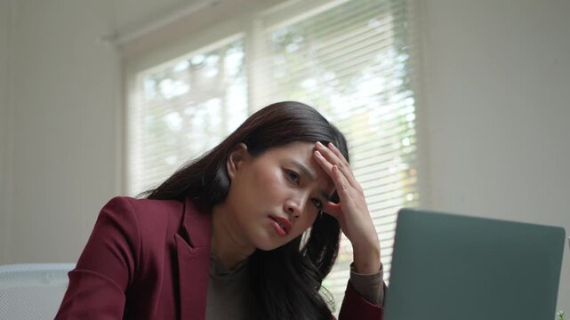 Young Asian businesswoman feeling tired and stressed from overworking. Frustrated female employee massaging her temples suffering from a headache