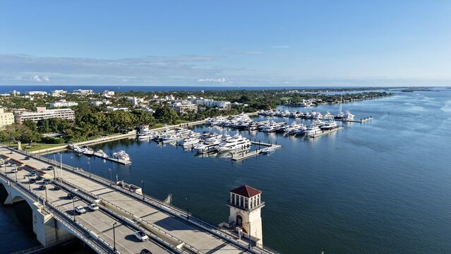 Aerial view of the Royal Park Bridge and a marina filled with luxury yachts under a clear blue sky in Palm Beach, Florida, United States.