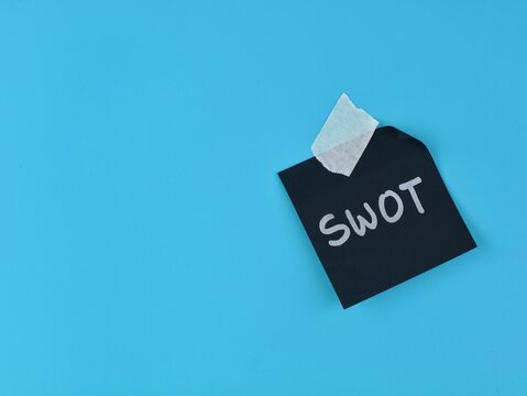 SWOT analysis word written on black note paper with adhesive tape on blue background. Concept for business marketing strategy, corporate planning, project assessment, and analysis framework