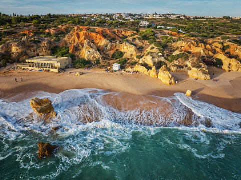 Drone view of waves curling along the beach below golden limestone cliffs at Praia de Sao Rafael beach.