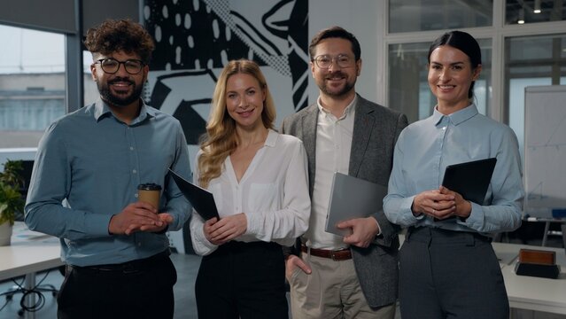 Multiethnic business team posing in office four multiracial businesspeople diversity colleagues standing in company agency firm smiling together businesswomen with businessman smile looking at camera