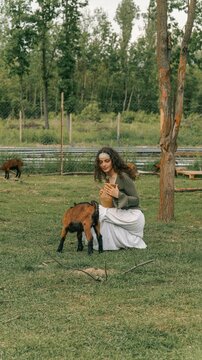 Young woman in traditional dress interacting with a goat in a grassy field