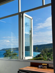 POV from inside a room looking through an open white window to a stunning tropical ocean view with palm trees and hills © Muhammad