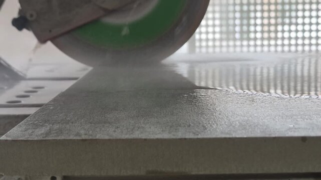 Side view of a wet tile saw starting to cut a ceramic floor tile in slow motion.