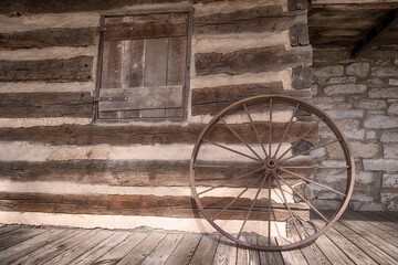 Fototapeta premium Rustic old wagon wheel leaned against a log cabin wall.