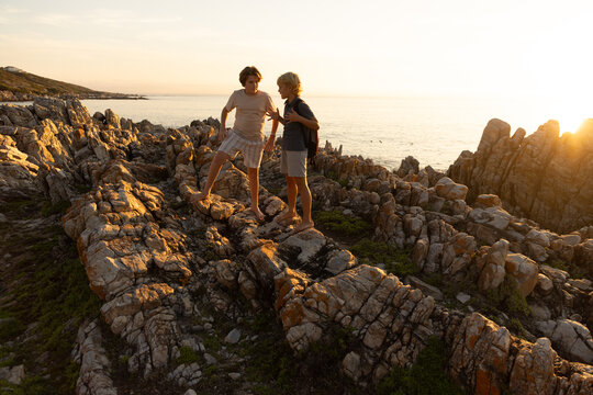 2 pre teen boys climbing and exploring rocky coastline of DeKelders, South Africa