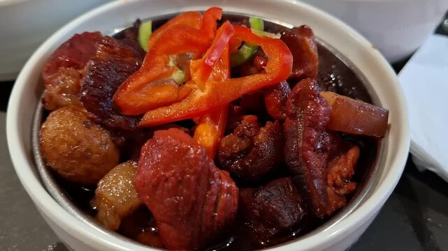 Traditional red braised pork belly or Hong Shao Rou served in white ceramic bowl. Tender meat chunks topped with fresh sliced red bell pepper. Asian food concept. Authentic Chinese cuisine dish