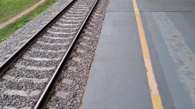 Industrial background straight railroad tracks along grey asphalt empty passenger platform edge. Railway line infrastructure for transportation, travel, logistics. Metal train rails, concrete sleepers