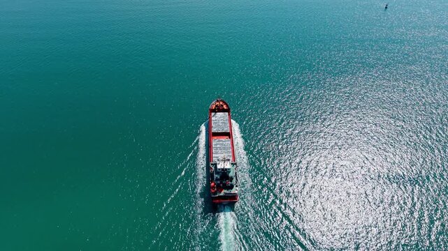 Large cargo vessel cruising through open turquoise water. Following a ship on the vast seascape. Top view.