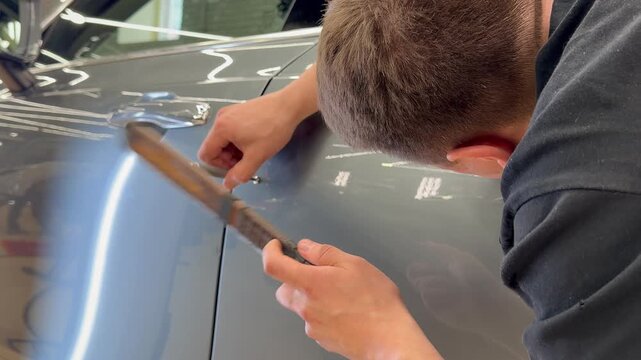 PDR. The mechanic at the auto shop with tools to repair dents in car body. Body repair. A specialist repairs a dent on the car body without painting. Paintless Car Dent Repair. 