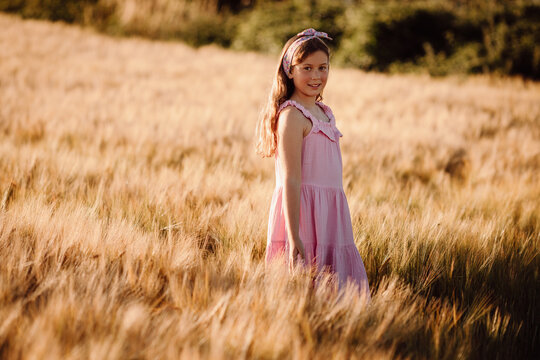 girl looking back over shoulder while standing in tall golden barley