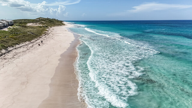 Aerial view of the pristine white sands of Stocking Island Beach meeting turquoise ocean waves under a bright sky in Exuma, Exuma, The Bahamas.