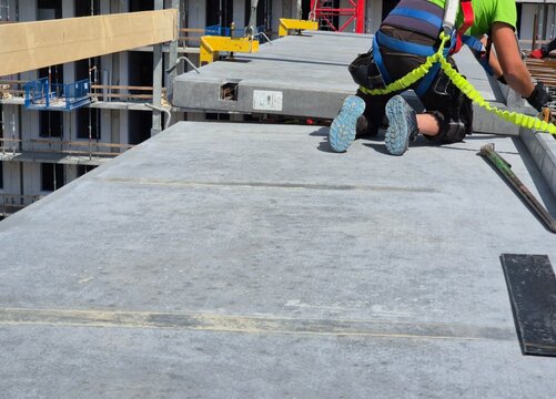 Rear view of a worker in proper PPE and fall protection installing a precast balcony panel.