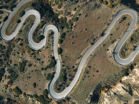 Aerial view of a winding serpentine road snaking through a hilly landscape with sparse vegetation and dry shrubs in Petrolla, Basilicata, Italy.