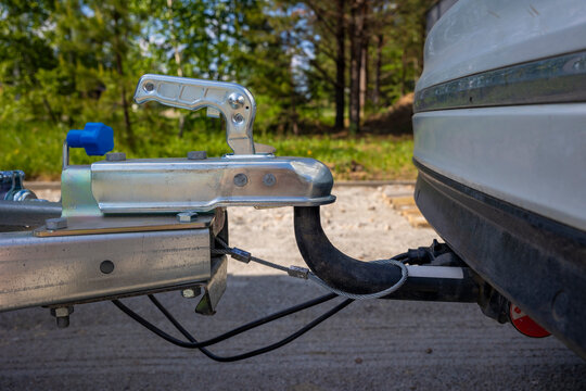 Close up of a metallic trailer hitch coupler attached to a car tow ball outdoors. Concept: safe towing connection