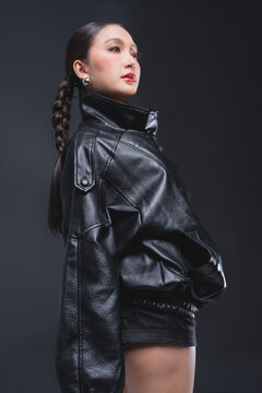 Side profile of Asian woman looking over shoulder in leather jacket for high fashion cosmetics marketing campaign luxury streetwear aesthetic urban lifestyle edgy portrait studio