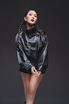 Full length of Asian fashion model in leather jacket and boots for luxury outerwear marketing campaign cyber punk aesthetic modern urban lifestyle confident posing studio