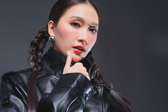 Low angle of confident Asian woman in leather jacket for high fashion cosmetics marketing campaign luxury streetwear aesthetic female empowerment concept edgy portrait studio