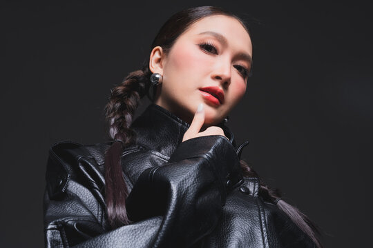 Mysterious Asian woman covering half face in leather jacket for high fashion cosmetics skincare marketing campaign intense eye contact dualism concept edgy portrait studio