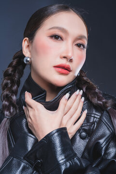 Low angle of confident Asian woman in leather jacket for high fashion cosmetics marketing campaign luxury streetwear aesthetic female empowerment concept edgy portrait studio