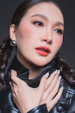 Low angle of confident Asian woman in leather jacket for high fashion cosmetics marketing campaign luxury streetwear aesthetic female empowerment concept edgy portrait studio