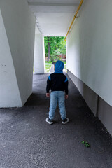 Fototapeta premium Little boy stands in a concrete open tunnel. Child under the supporting structure of a building