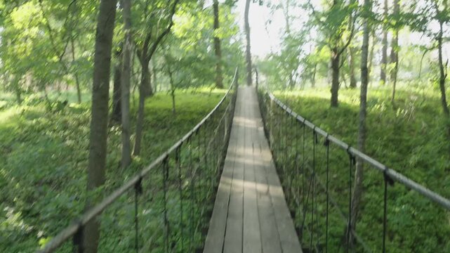 The camera moves across a suspension bridge over a ravine