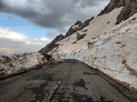 Spring mountain road carved between tall snow walls in Tette heights, showing melting layers and rugged slopes under a dramatic cloudy sky.
📍Tatte, Hawraman Takht, Kurdistan 