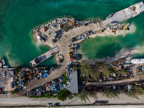 Aerial view of heavy machinery and industrial barges at Arawak Cay with turquoise waters and coastal vegetation in Nassau, New Providence, The Bahamas.