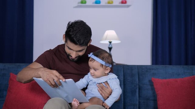 A smart young father with his little daughter - reading a book  new skill  social development. A young and charming father and his little baby girl having a good time together at home - leisure tim...