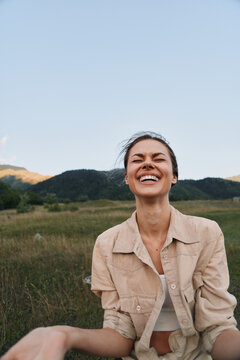 Woman outdoors, smiling with eyes closed, sunlit field background, casual jacket, relaxed lifestyle, natural colors, joyful moment, fresh air, carefree mood, outdoors vibe