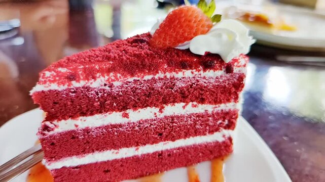 A slice of delicious red velvet cake, layered with cream and topped with a strawberry and whipped cream. The cake is garnished with a strawberry syrup drizzle, making it an appealing dessert