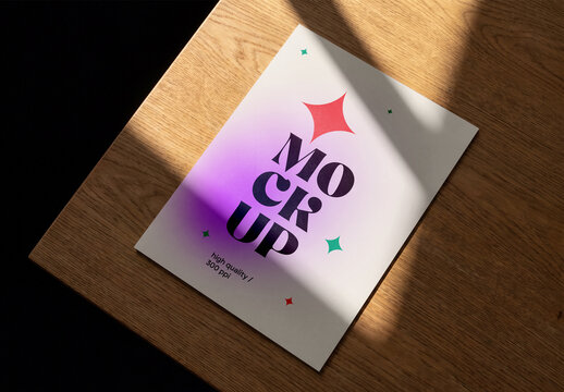 High-angle shot of a blank flyer or poster mockup lying on a wooden table with harsh light and shadows cast across the surface