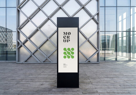 Front view of a vertical black outdoor digital signage totem mockup standing on a wooden deck in front of a modern glass building facade