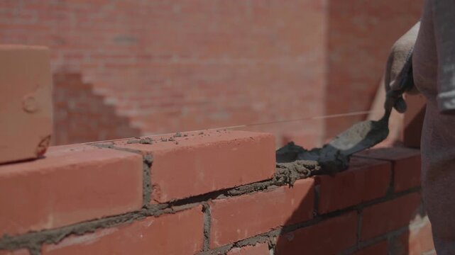 Close-up of a construction worker gloved hands, laying red bricks with wet cement. Professional bricklayer at the construction site.