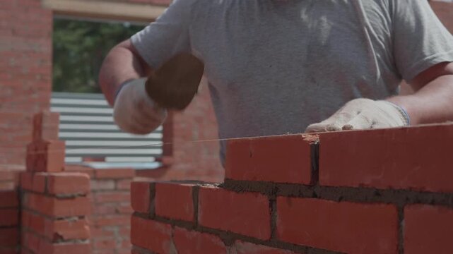 Close-up of a construction worker gloved hands, laying red bricks with wet cement. Professional bricklayer at the construction site.