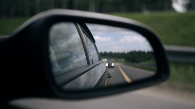 The side rearview mirror reflects the highway and cars. Filmed in motion