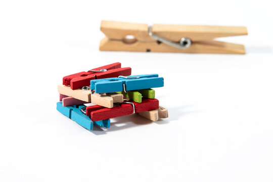 A square arrangement of colorful blue, green, and red wooden clothespins with one large natural wooden clothespin lying in the background on a clean white background