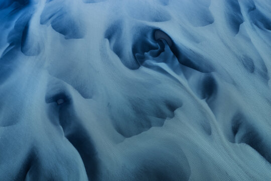 Aerial view of abstract patterns and textures of a glacial braided river delta with blue water and grey sediment in Thorshofn, Langanesbyggd, Iceland.