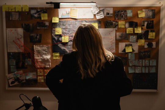 Female Detective near board with evidence in investigation office working clue map. Crime and case criminal leads