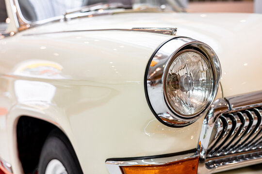 Close-up of the round headlamps of a white classic car. Beautifully restored chrome details of a historic vehicle. Round headlight of a white old timer car