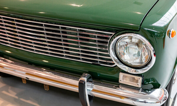 Close-up of the round headlights of a green classic car. Beautifully restored chrome parts of a historic vehicle. Round headlight of a green vintage car.
